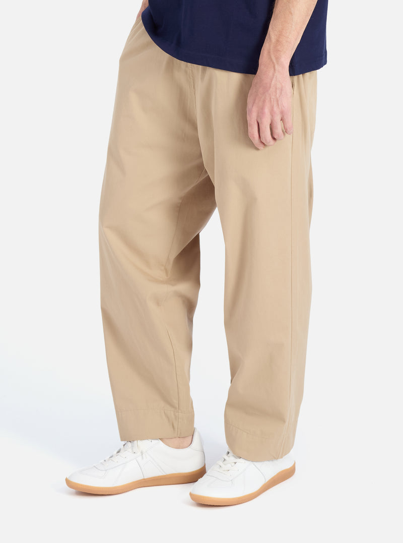 A man models the Sand Military Cotton Judo Pant in a studio setting. The pants are a relaxed fit and paired with white sneakers. The background is a clean, bright white.