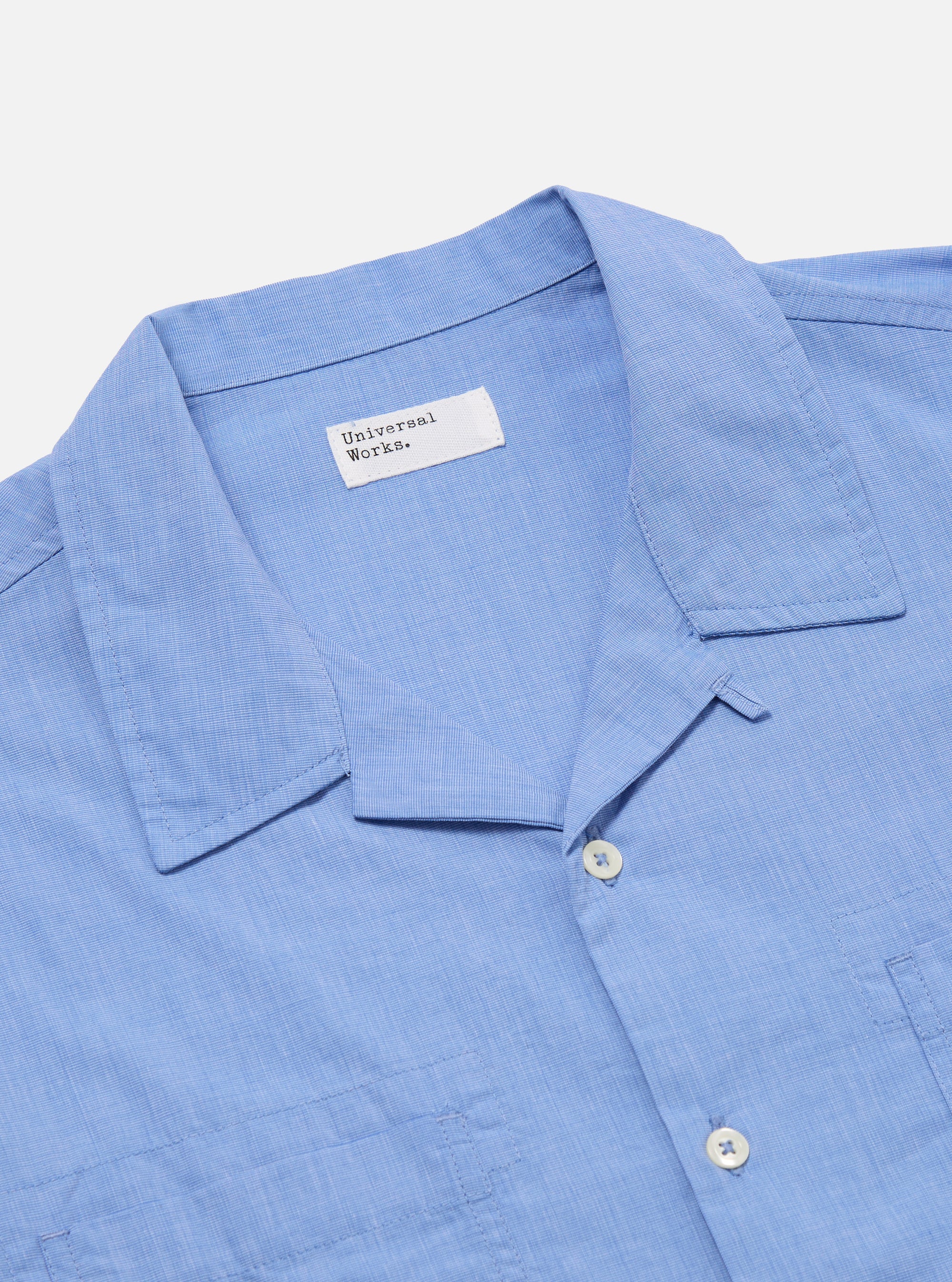 Close-up of the Blue End On End Cotton Garage Shirt on a white surface. The light blue cotton shirt has a collar, buttons, and chest pockets.