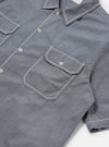 Close-up of the Grey End On End Cotton Utility SS Shirt on a white surface. The shirt features white stitching details on the pockets, collar, and sleeves.