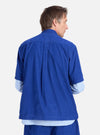 Back view of a man in the Work Blue Summer Cord Tech Overshirt. The corduroy overshirt is layered over a striped shirt. Shot against a white backdrop.
