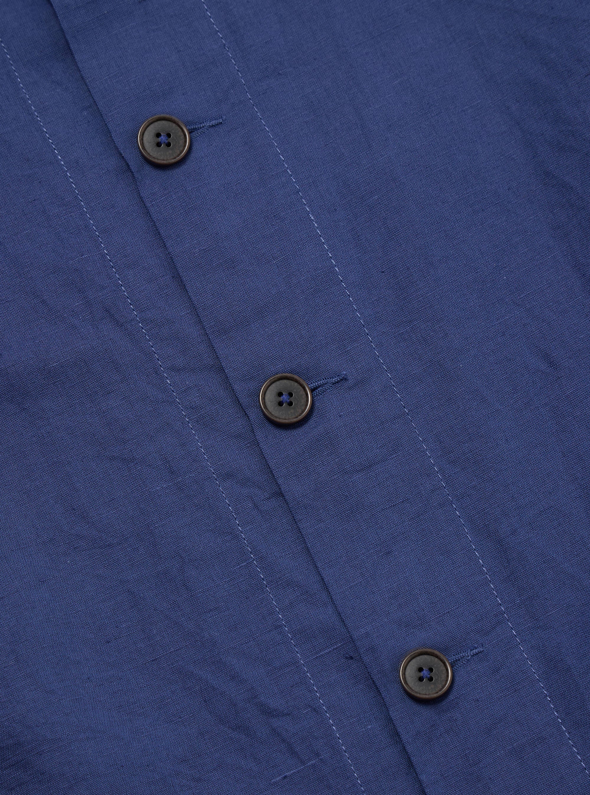 Close-up of the Blue Linen Cotton Shirting Travail Overshirt, showing the blue linen-cotton blend fabric and button details. The overshirt is neatly laid out on a flat surface.
