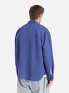 Back view of a model wearing the Blue Linen Cotton Shirting Travail Overshirt. The overshirt is styled with light blue pants against a clean white backdrop.