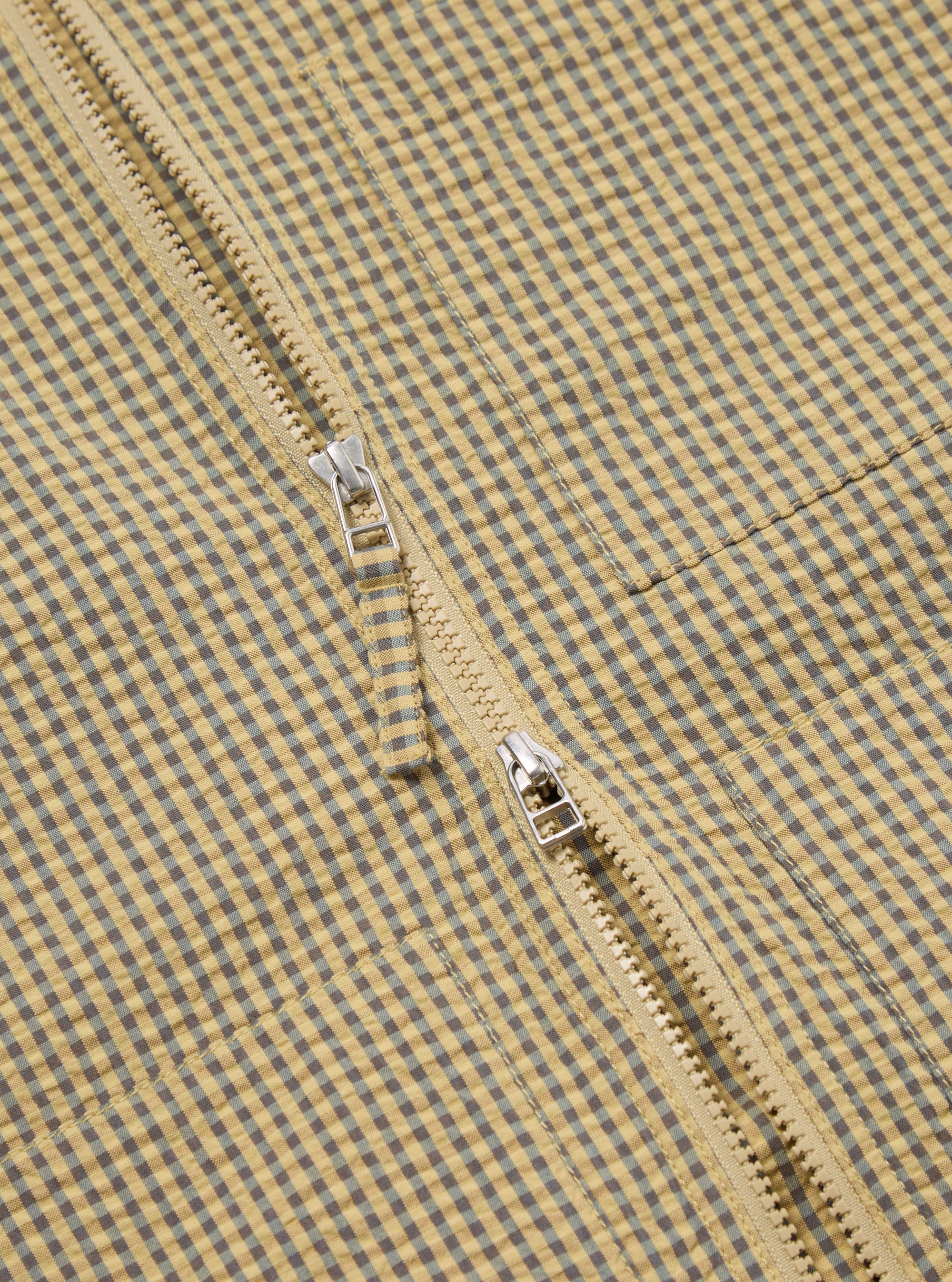 Close-up of the Yellow Japanese Seersucker Zip Uniform Jacket, showcasing its yellow and blue checkered pattern and zipper detail. The jacket is laid flat on a neutral surface.
