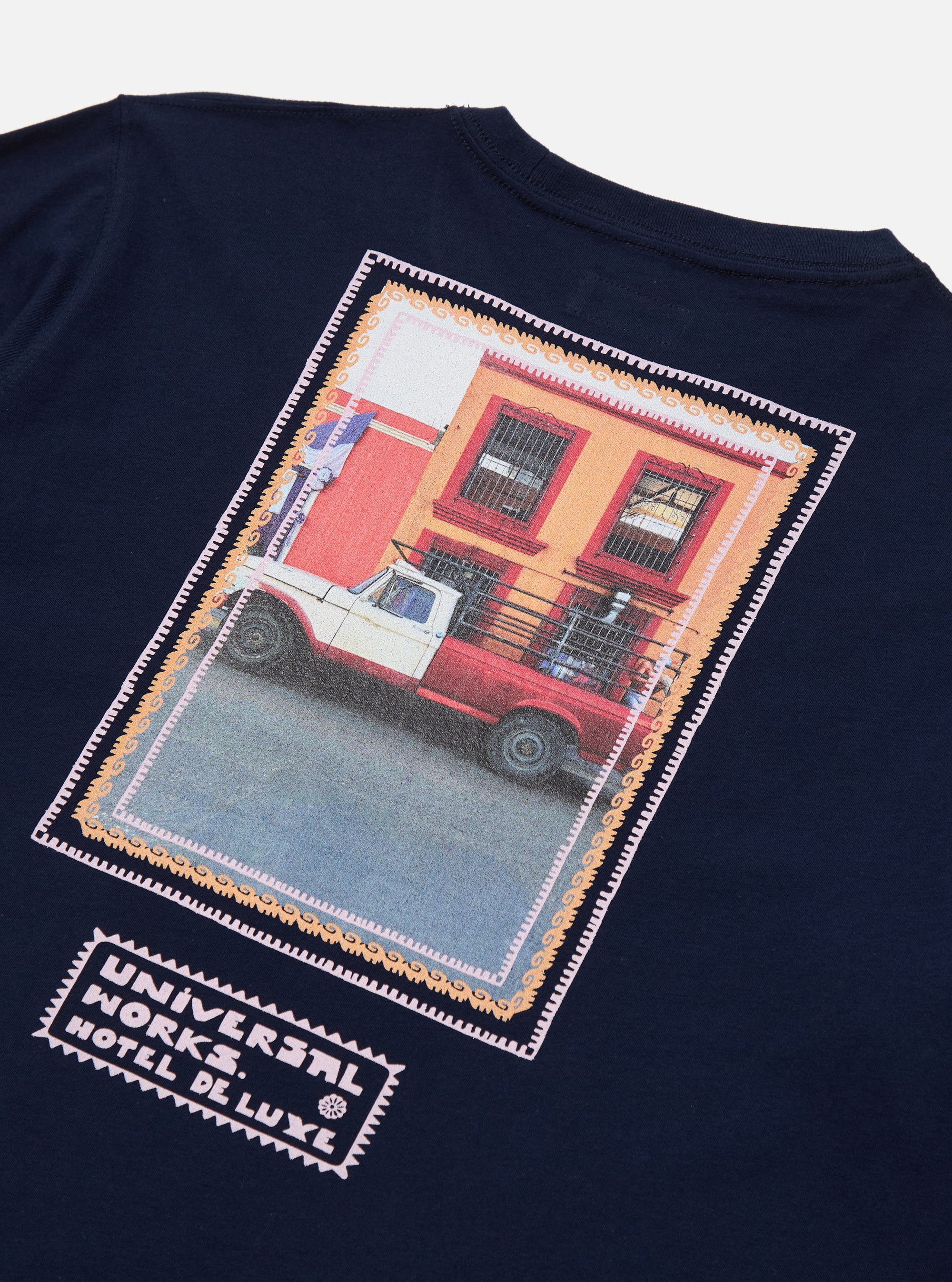Close-up of the Navy/Pink Single Jersey Pickup Print Tee. The tee is navy with a pink-bordered print of a pickup truck in front of a building. 