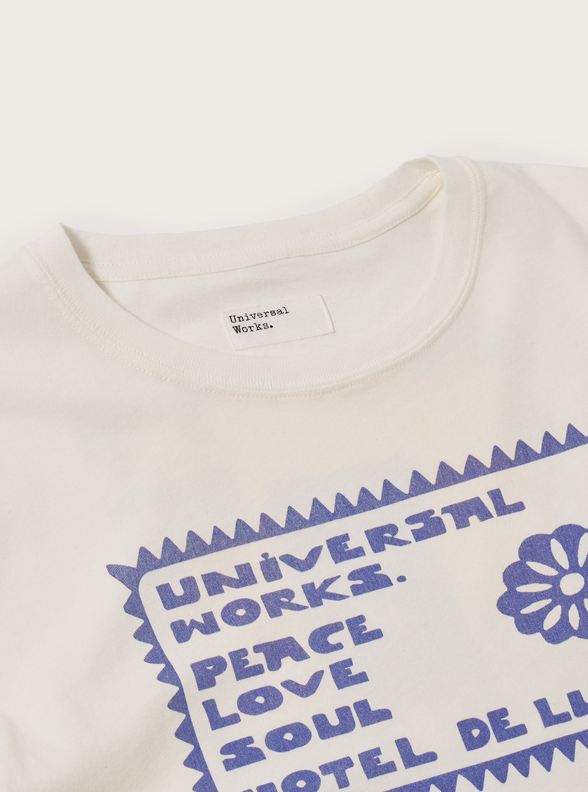 Close-up of the Ecru/Yellow Single Jersey Pickup Print Tee on a white surface. The tee is ecru with a yellow print. The image focuses on the collar and upper chest.