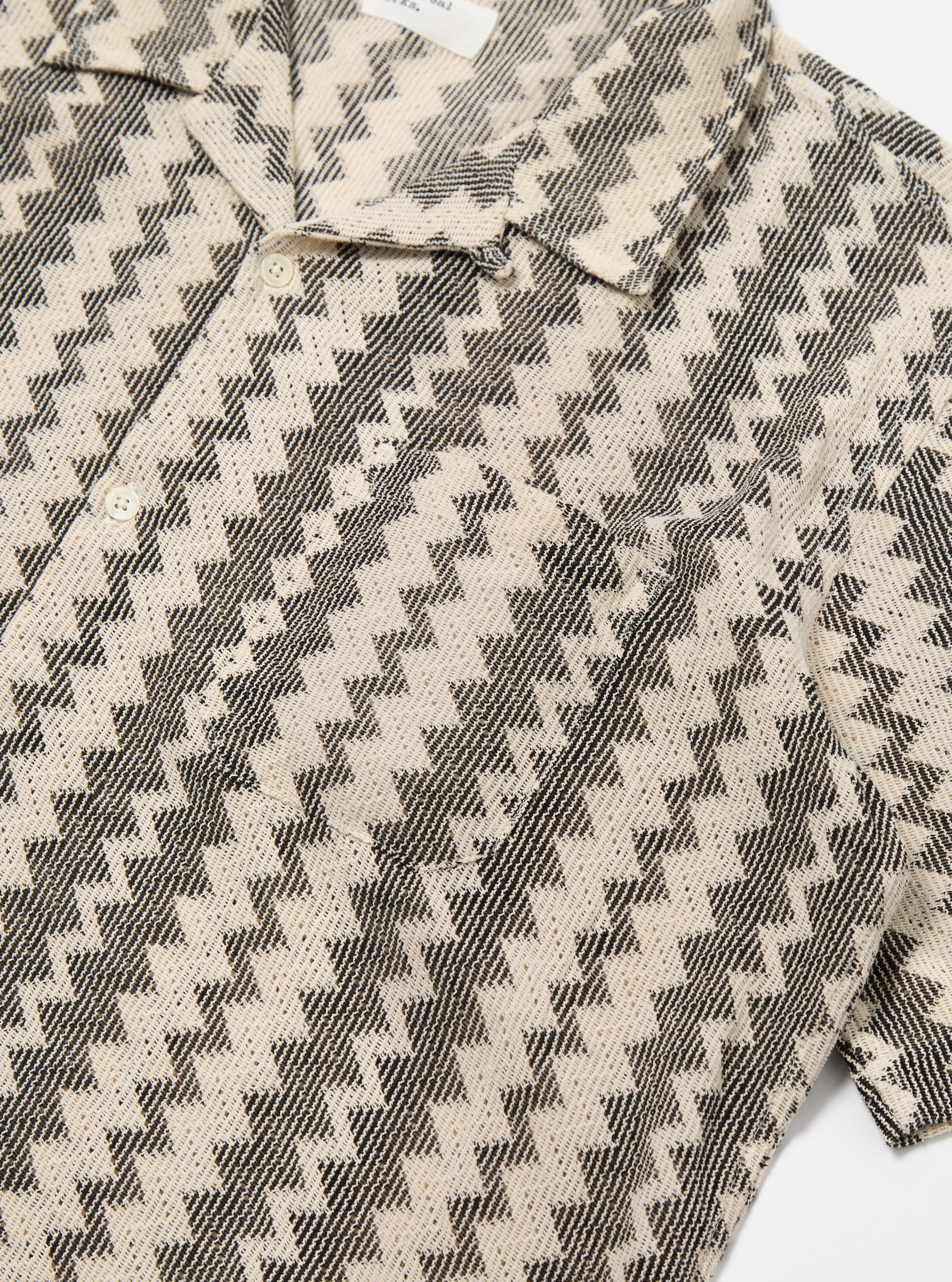 Close-up of the Charcoal Cotton Lattice Road Shirt on a white surface. The shirt has a black and cream lattice pattern and short sleeves.