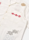 Close-up of the ecru poplin Minari shirt with red and gold embroidery on a white background. The shirt has a camp collar and a chest pocket.