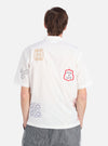 Back view of a model wearing the Ecru Embroidered Poplin Minari Shirt. The shirt is ecru with colorful embroidery. Shot against a white background.