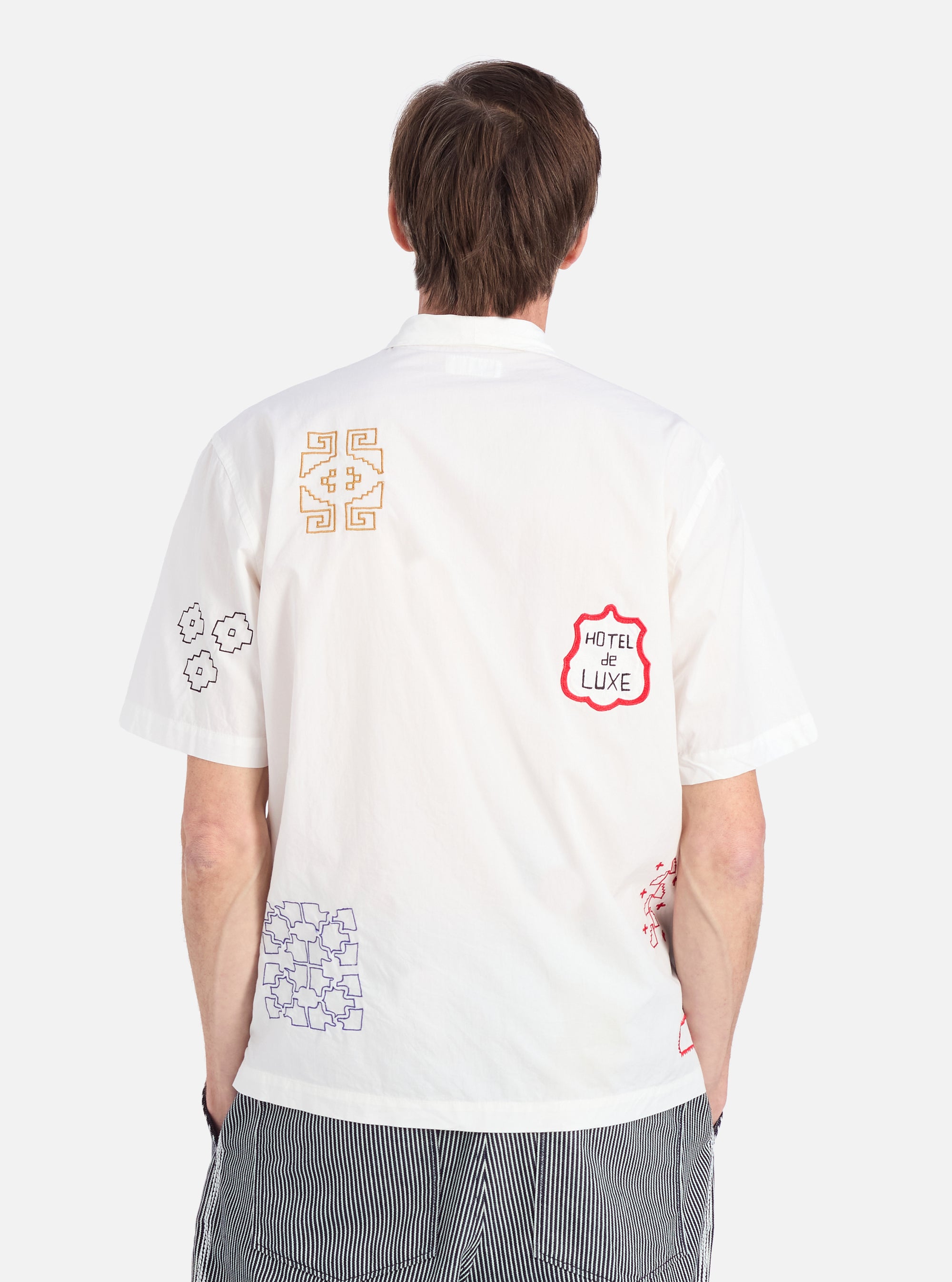 Back view of a model wearing the Ecru Embroidered Poplin Minari Shirt. The shirt is ecru with colorful embroidery. Shot against a white background.