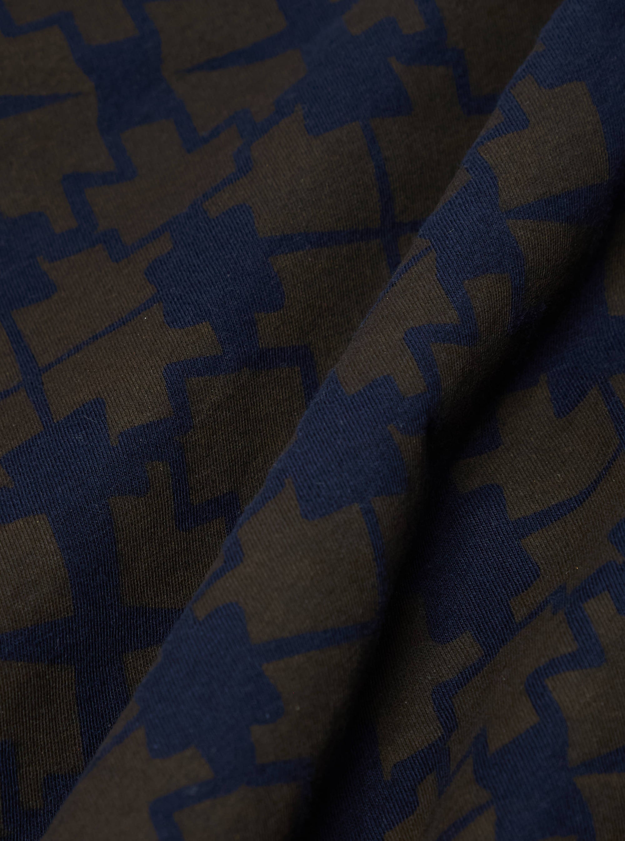 Close-up of the Navy/Brown Mitla Print Jersey Newlyn Polo fabric. The jersey material features a geometric print in navy and brown hues.