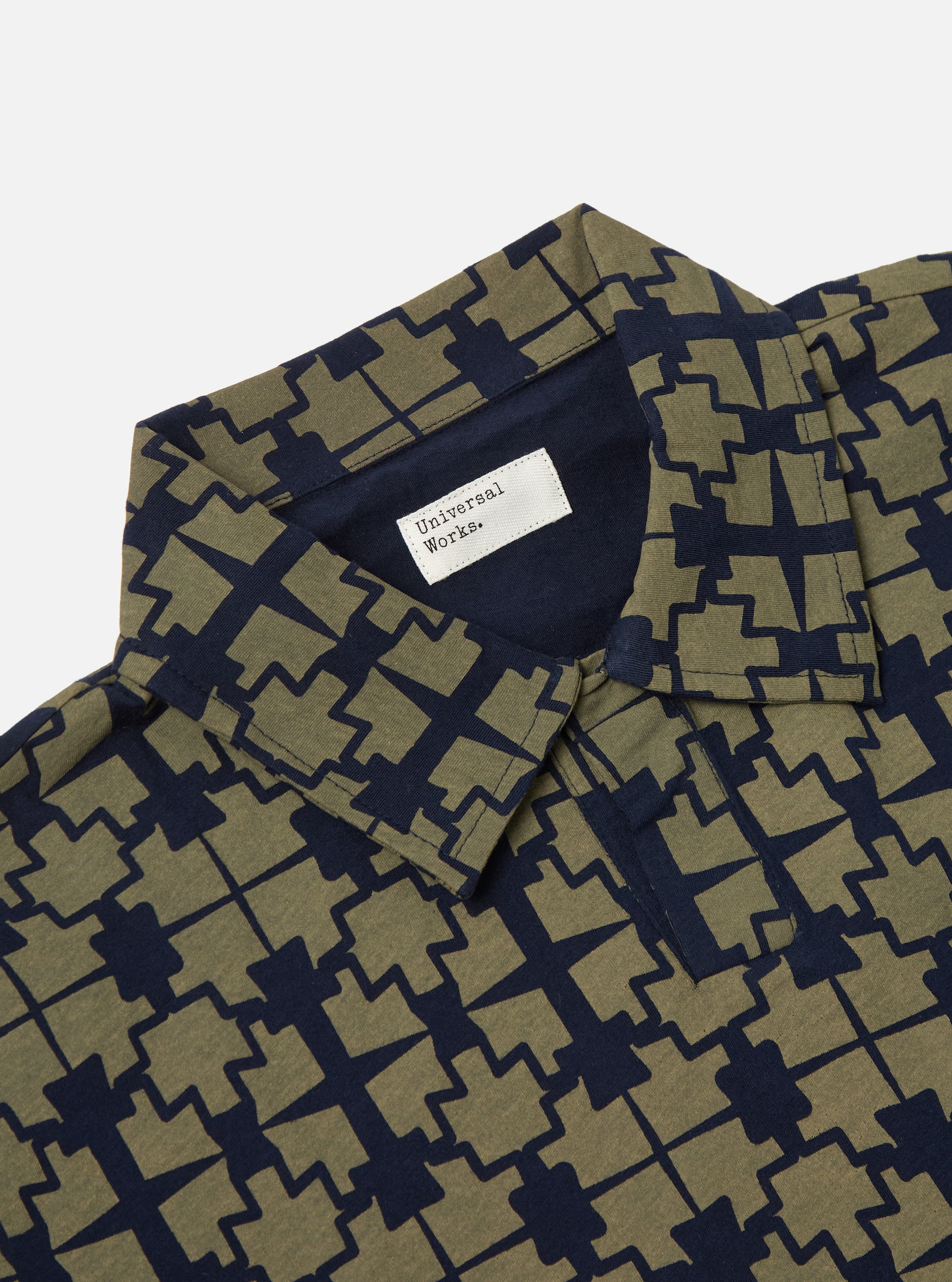 Close-up of the Navy/Mud Mitla Print Jersey Newlyn Polo on a white background. The polo shirt features a navy and mud-colored geometric print.
