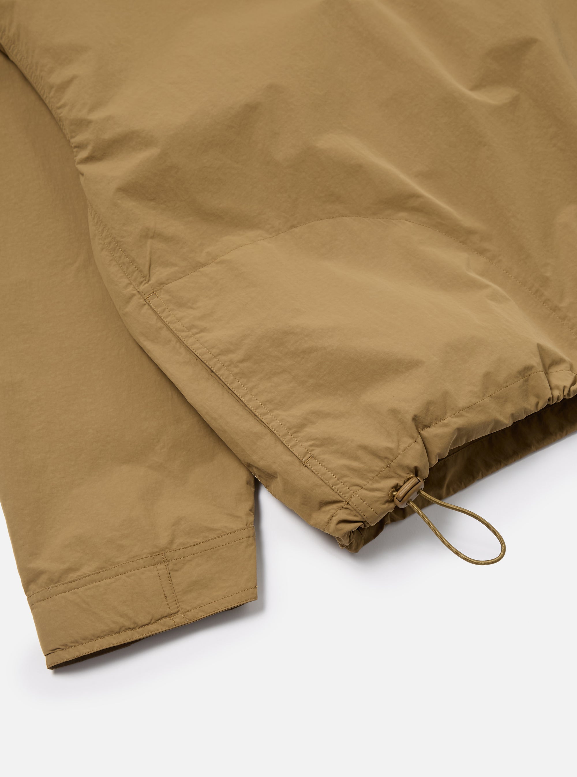 Close-up of the Dark Sand Peach Recycled Nylon Liam Jacket. Shows the sleeve and hem detail with drawstring. The jacket is on a white surface.