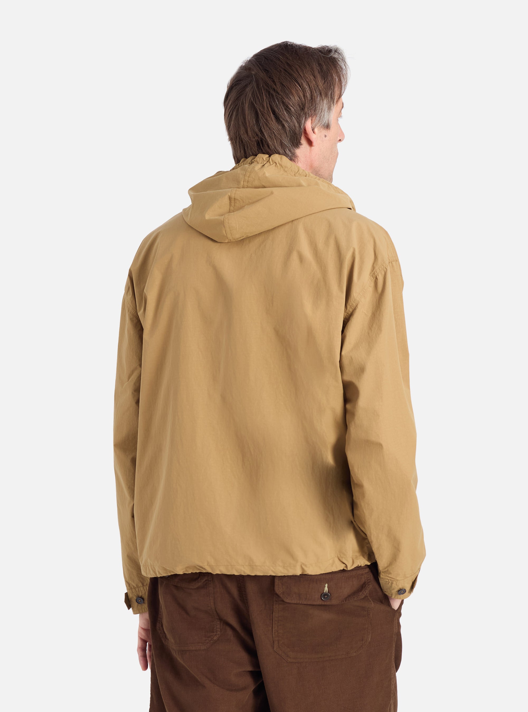 Back view of a model wearing the Dark Sand Peach Recycled Nylon Liam Jacket. The jacket is paired with brown corduroy pants. The background is a clean, bright white.