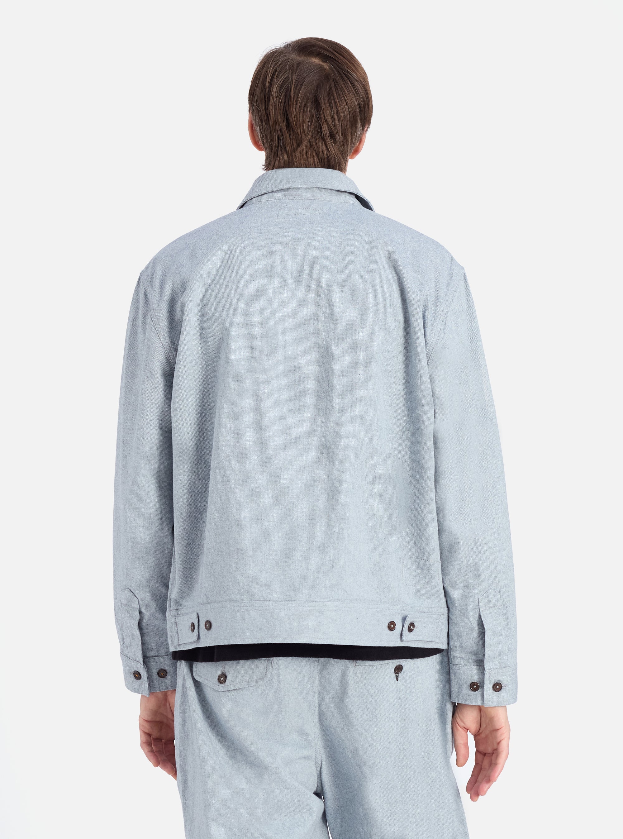Back view of a model wearing the Indigo Reworked Jean Cloth Rose Bowl Jacket and matching pants. Light blue denim material with brown buttons. Shot against a white background.