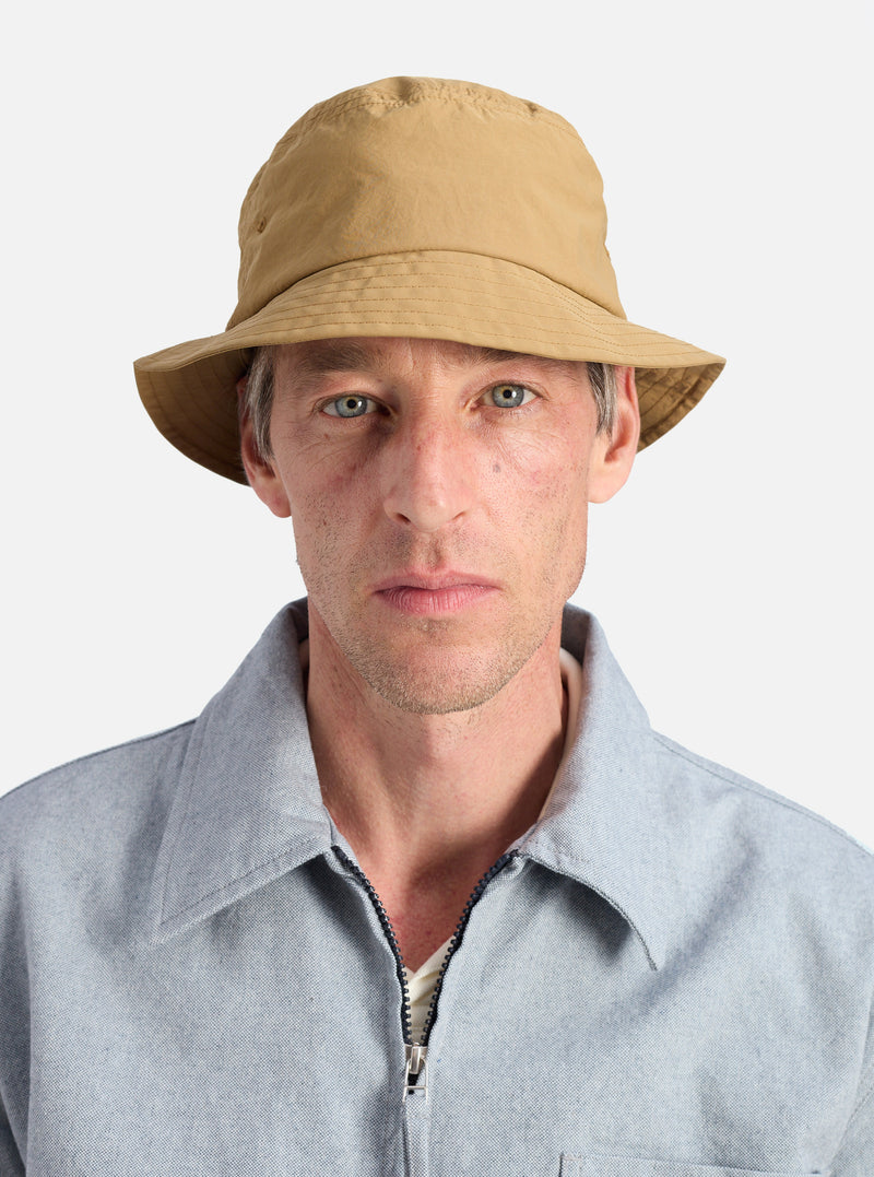 A model wears the Dark Sand Peach Recycled Nylon Beach Hat against a white background. The hat is a light tan color and made of a lightweight material.