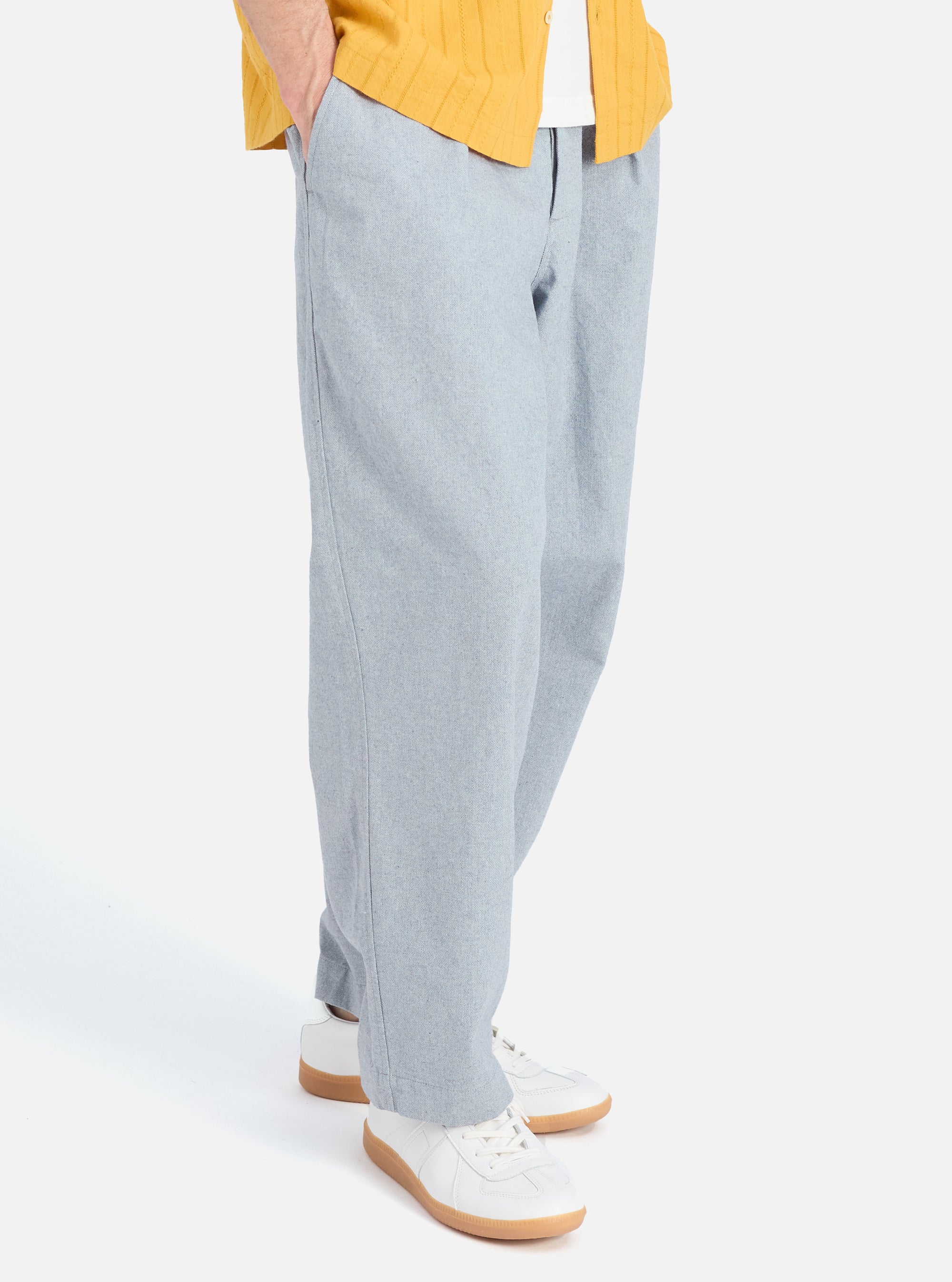 A model wears the Indigo Reworked Jean Cloth Oxford Pant, a light blue, loose-fitting trouser. Shot in a studio setting with a white background.