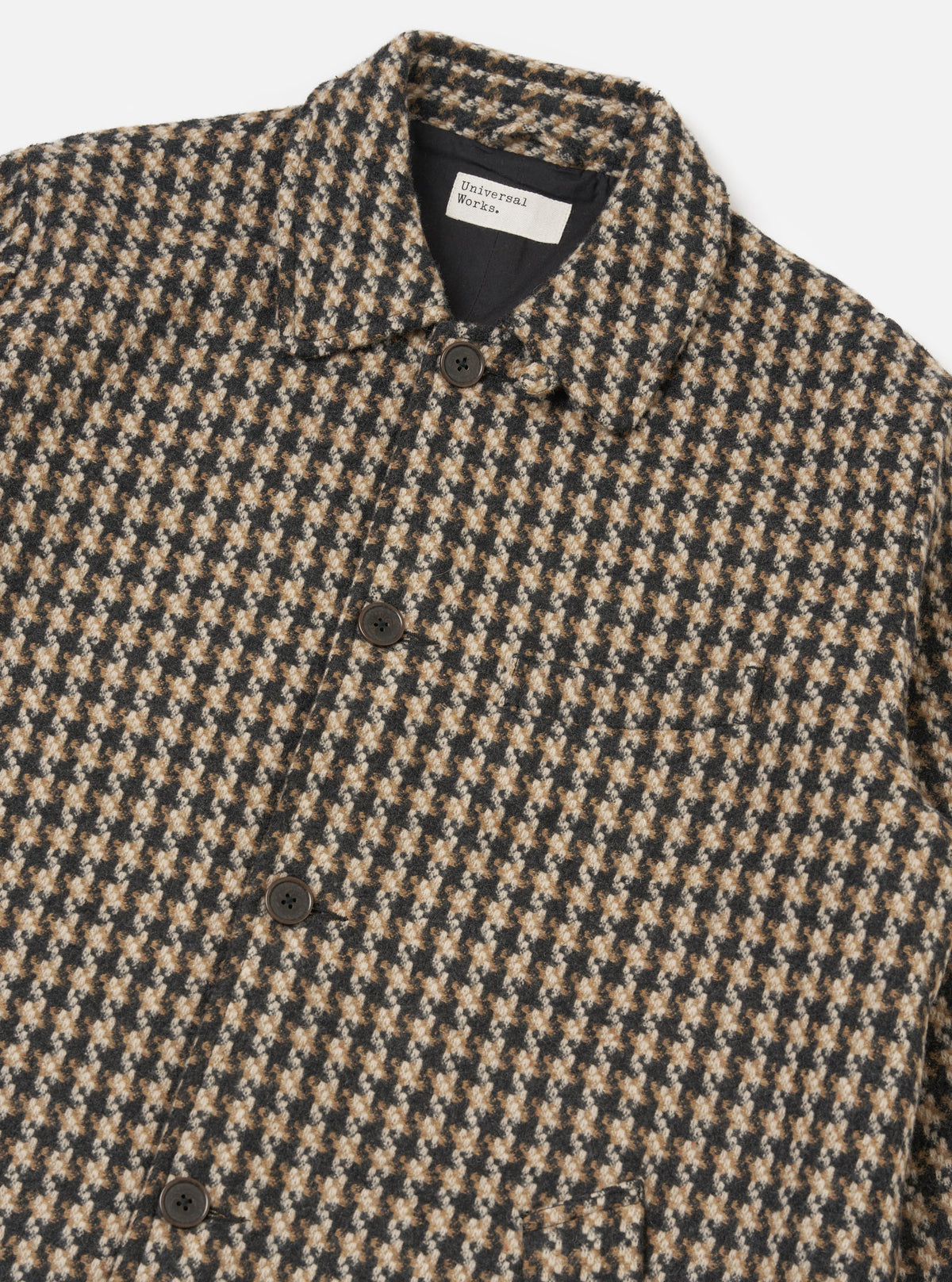 Close-up of the Sand Cortina Tweed Long Swing Coat. The tweed is a houndstooth pattern in sand, brown, and black. The coat is buttoned and laid on a white surface.