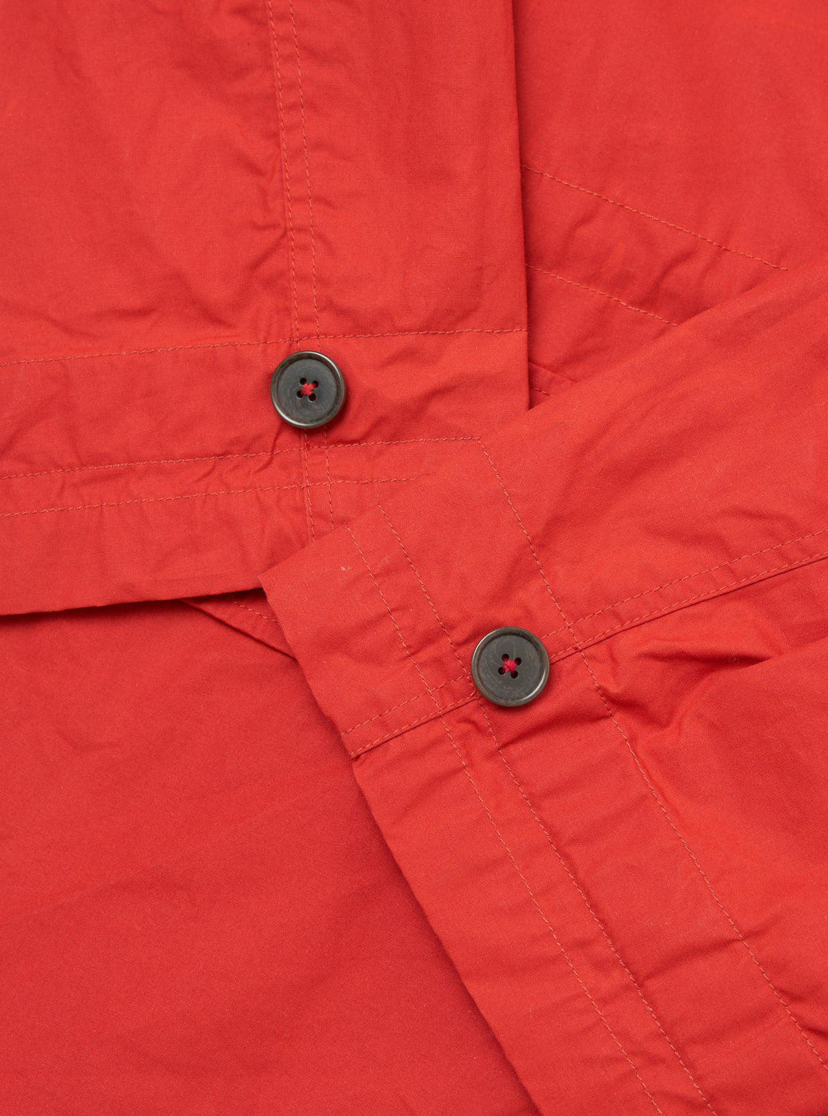 Close-up of the Orange British Wax Cotton Boston Parka showing the texture of the fabric, button details, and stitching. The image is taken on a flat surface.