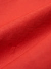 Close-up of the Orange British Wax Cotton Boston Parka fabric. The durable material is displayed on a plain background, highlighting the texture and vibrant color.