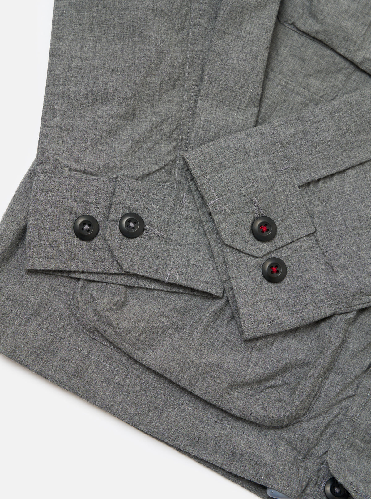 Close-up of the Charcoal Organic Chambray Parachute Field Jacket on a white surface. The jacket features black buttons with red stitching. The chambray material has a subtle texture.