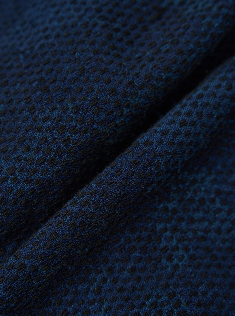 Close-up of the Black/Indigo Denim Camo Cabin Jacket fabric. The material is a textured blend of black and indigo threads, creating a subtle camo pattern.
