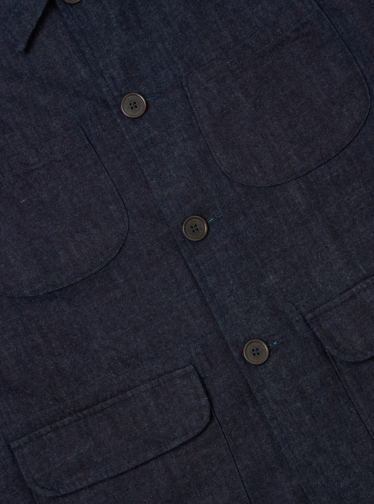 Close-up of the Indigo Brushed Denim Labour Jacket showing the brushed denim texture, pockets, and button details. The jacket is laid flat on a neutral surface.