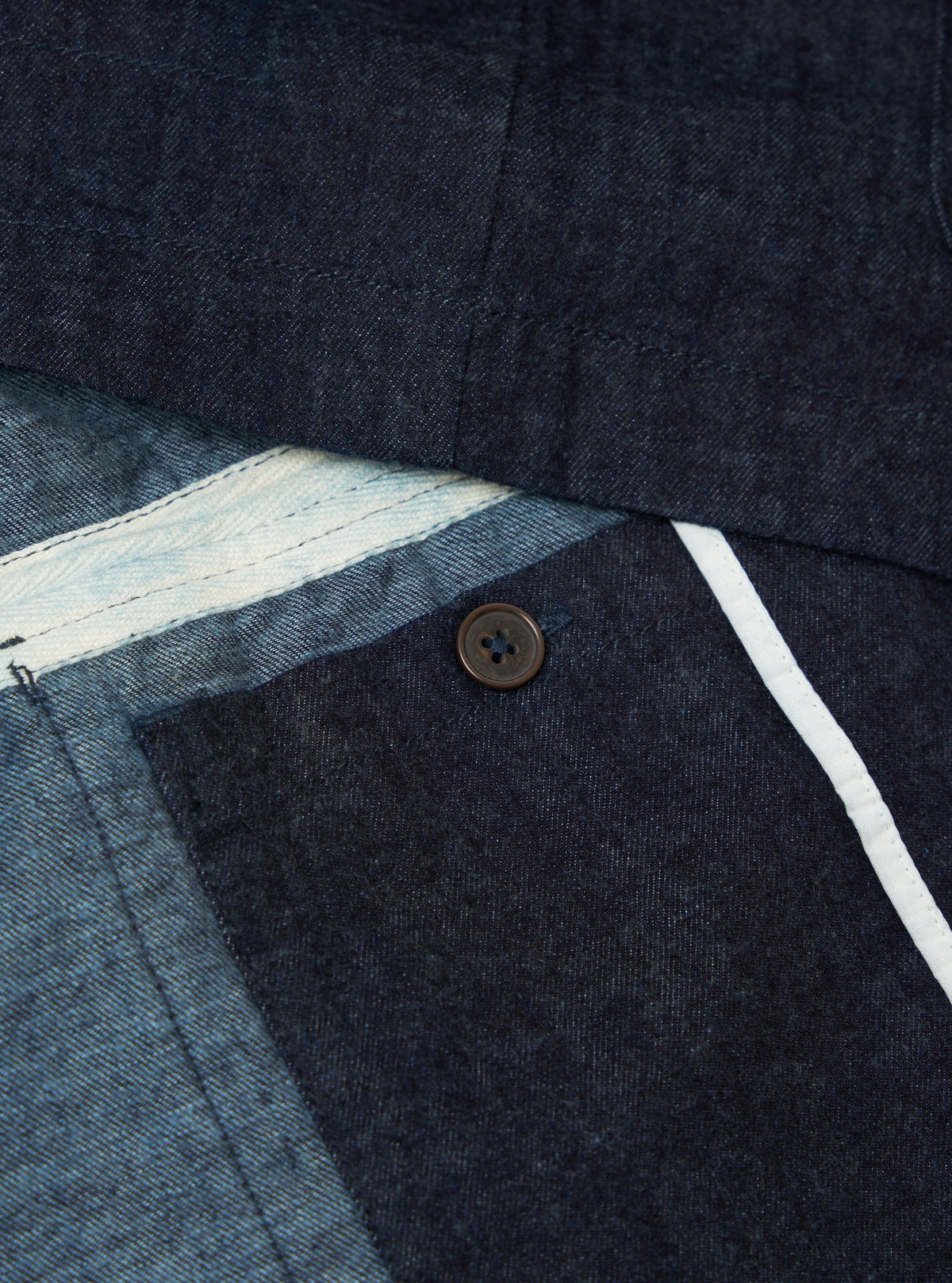 Close-up of the Indigo Brushed Denim Labour Jacket showing the denim texture, button, and white trim. The jacket is neatly arranged on a flat surface.