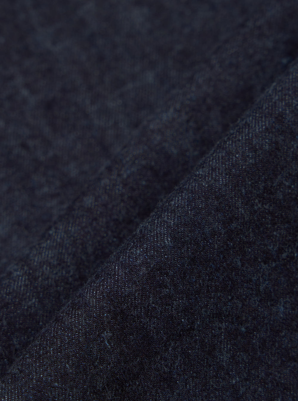 Close-up of the Indigo Brushed Denim Labour Jacket fabric. The brushed denim has a soft texture and rich indigo color. Shot on a simple background.