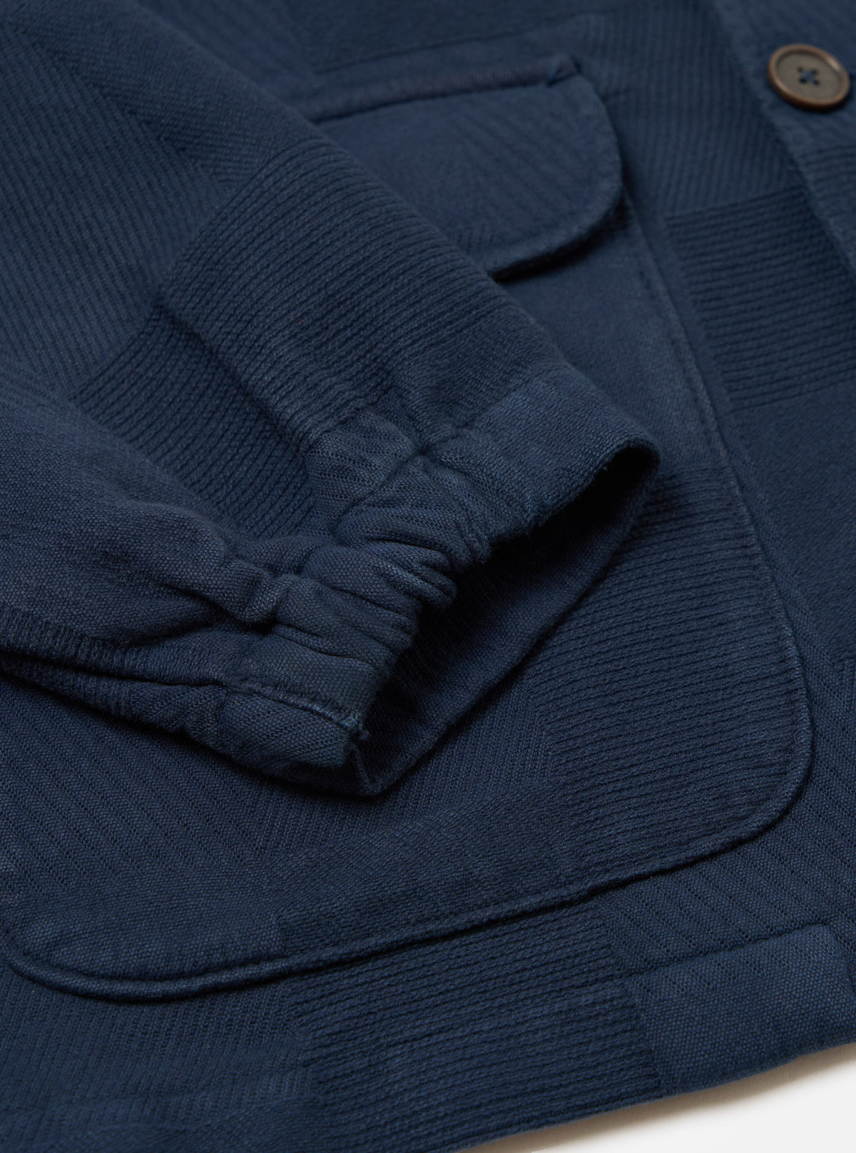 Close-up of the Dark Navy Patchwork Weave Cotton Labour Jacket showing the sleeve, pockets, and textured cotton weave on a white surface.