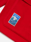 Close-up of the red Mowbray Military Fatigue Jacket showing the wool texture and a 'Hotel Deluxe' patch. The jacket is laid flat on a white surface.