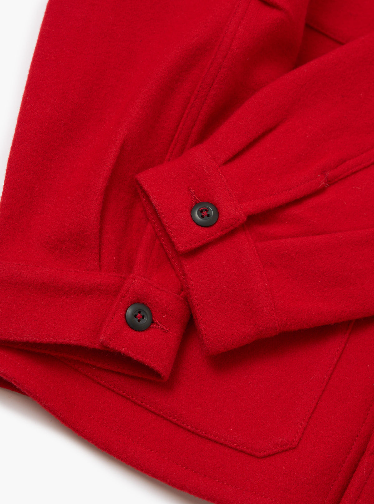 Close-up of the Red Mowbray Military Fatigue Jacket. The bright red wool fabric is detailed with black buttons. Shot on a white surface.