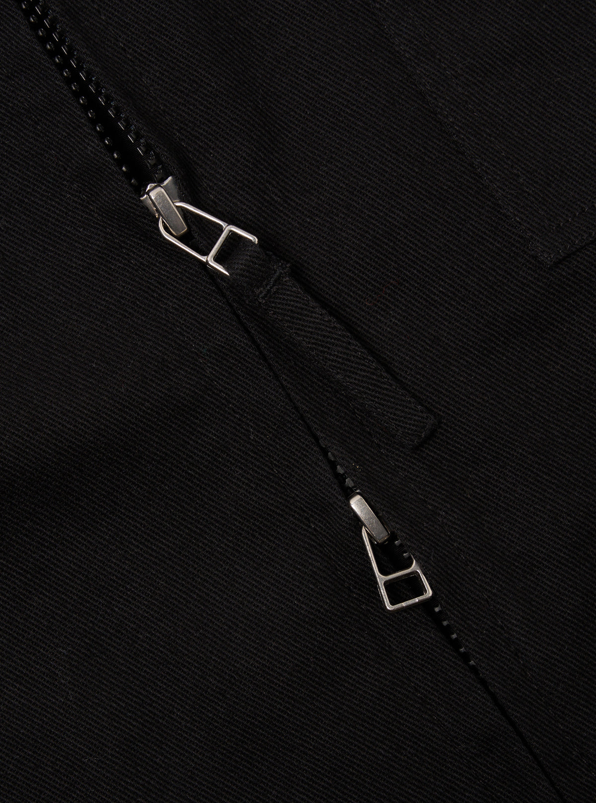 Close-up of the Black Works Twill Rose Bowl Jacket. The black twill fabric is visible, along with the jacket's zipper. The background is a plain, dark surface.