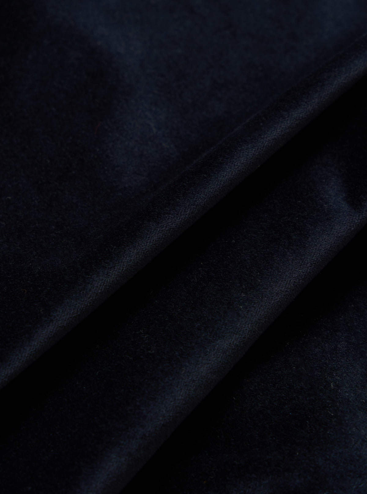 Close-up of the Navy Velveteen Two Button Jacket fabric. The rich, dark navy velveteen is draped to show texture. Studio shot on a neutral background.
