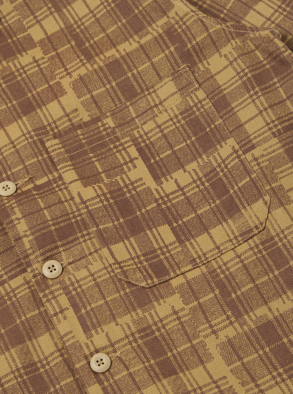Close-up of the Khaki Patch Check Twill Fatigue Shirt. The shirt features a brown and khaki check pattern, a chest pocket, and button closure. Shot on a flat surface.