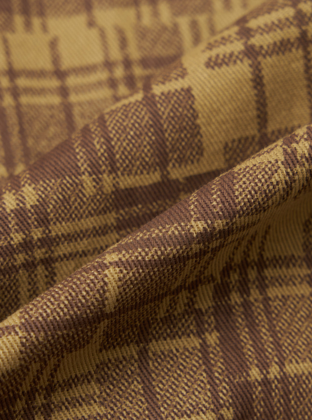 Close-up of the Khaki Patch Check Twill Fatigue Shirt fabric. The twill weave shows a khaki and brown check pattern. The fabric is draped to show texture.
