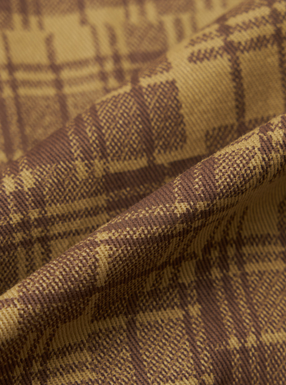 Close-up of the Khaki Patch Check Twill Fatigue Shirt fabric. The twill weave shows a khaki and brown check pattern. The fabric is draped to show texture.