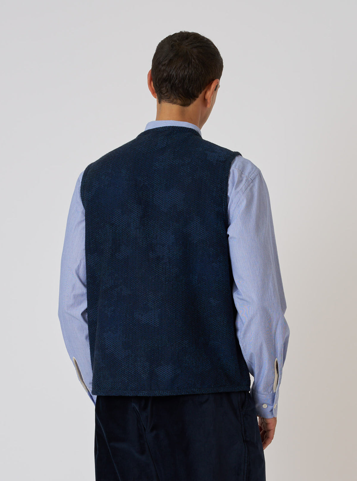 Back view of a model wearing the Black/Indigo Denim Camo 4 Pocket Gilet over a blue shirt. The gilet has a subtle camo pattern. Shot against a plain white backdrop.
