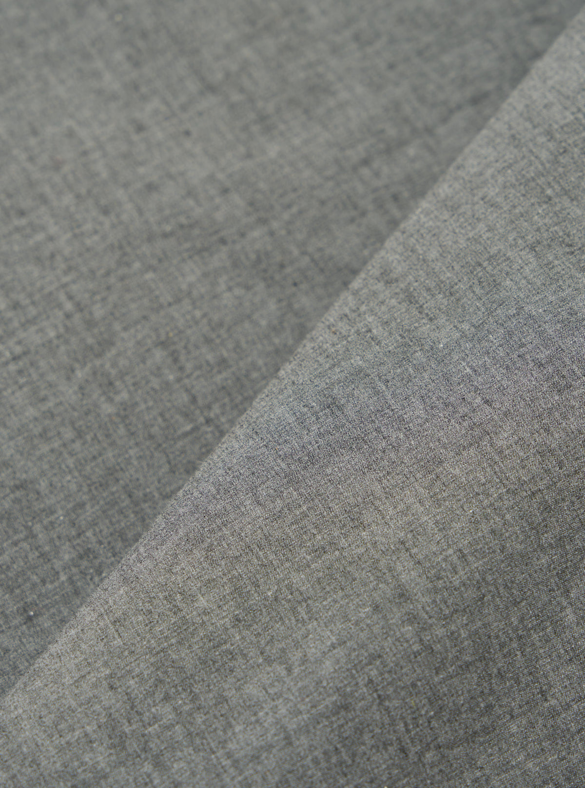 Close-up of the Charcoal Organic Chambray Parachute Liner Gilet fabric. The material is a woven chambray in a charcoal grey color. The fabric is folded to show texture.