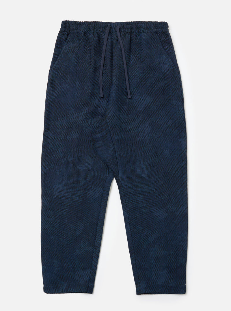 The Black/Indigo Denim Camo Braga Pant laid on a white surface. The pants are a relaxed fit with a drawstring waist and a subtle camo pattern.