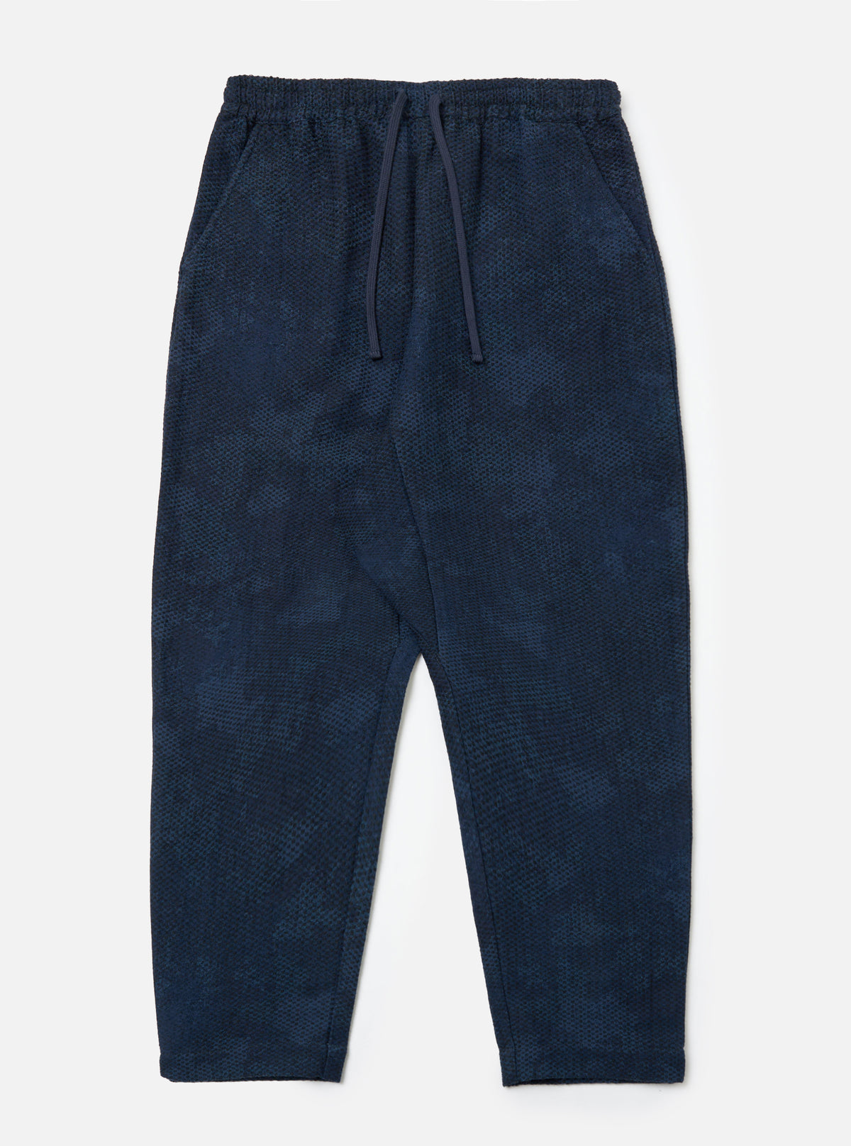 The Black/Indigo Denim Camo Braga Pant laid on a white surface. The pants are a relaxed fit with a drawstring waist and a subtle camo pattern.