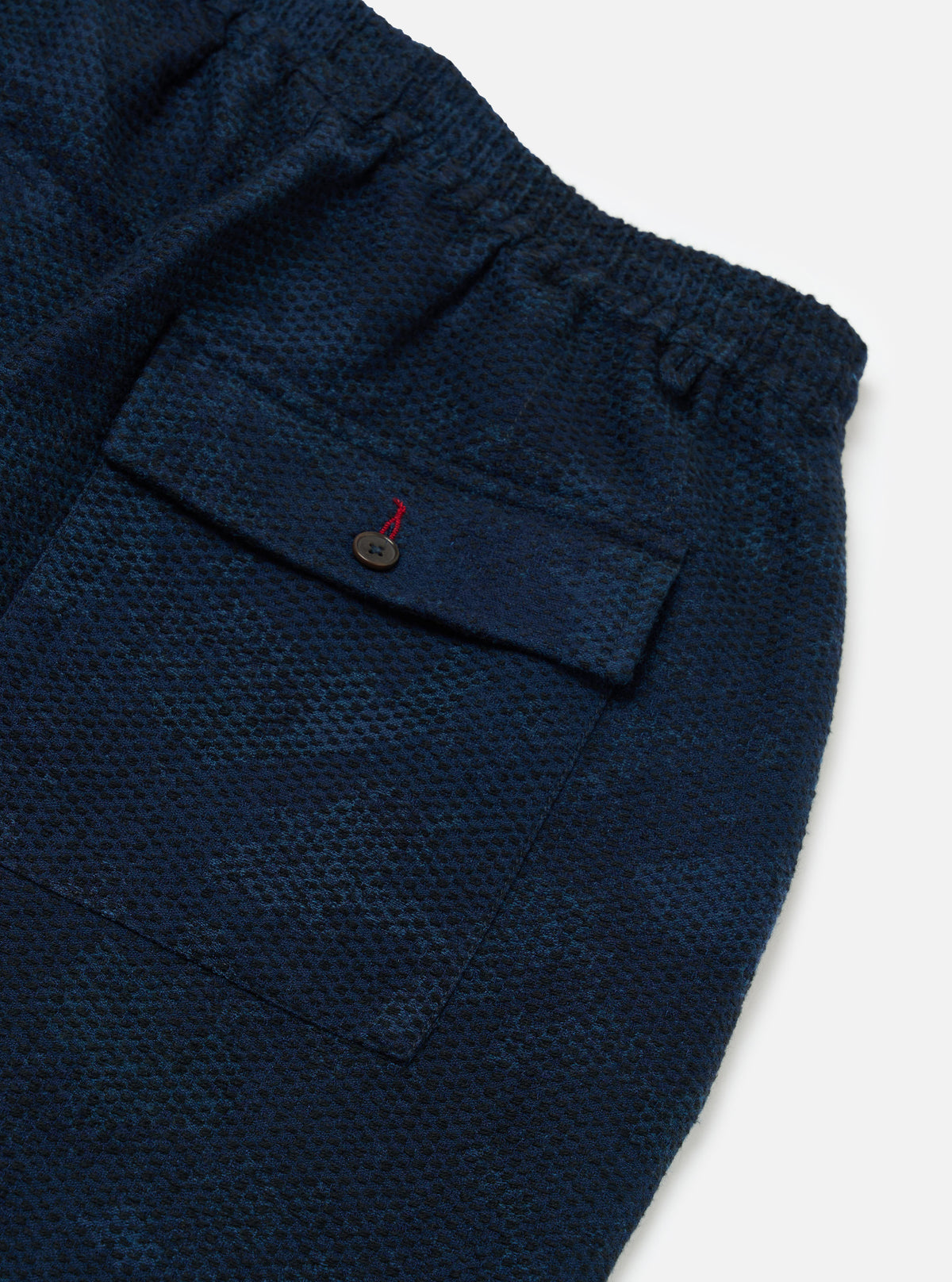 Close-up of the Black/Indigo Denim Camo Braga Pant on a white surface. The denim has a subtle camo pattern and a back pocket with a button closure.