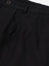 Close-up of the Black Organic Canvas Dutch Pant. Details include the button, belt loop, and pleats. The fabric is a dark canvas. Shot on a white background.