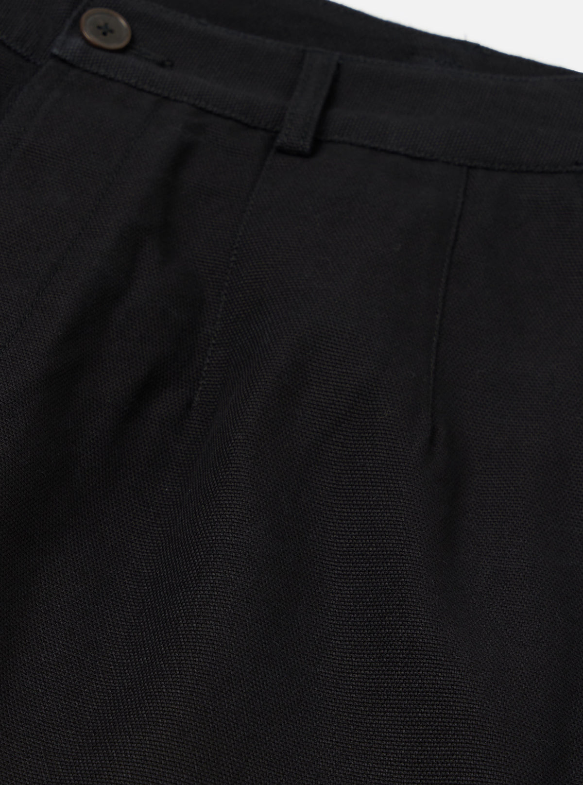 Close-up of the Black Organic Canvas Dutch Pant. Details include the button, belt loop, and pleats. The fabric is a dark canvas. Shot on a white background.