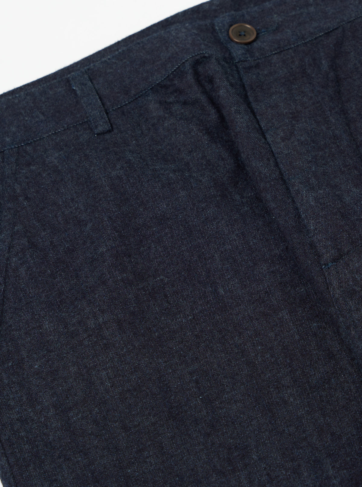 Close-up of Indigo Brushed Denim Military Chino on a white background. The dark wash denim shows the texture and details of the fabric and button.
