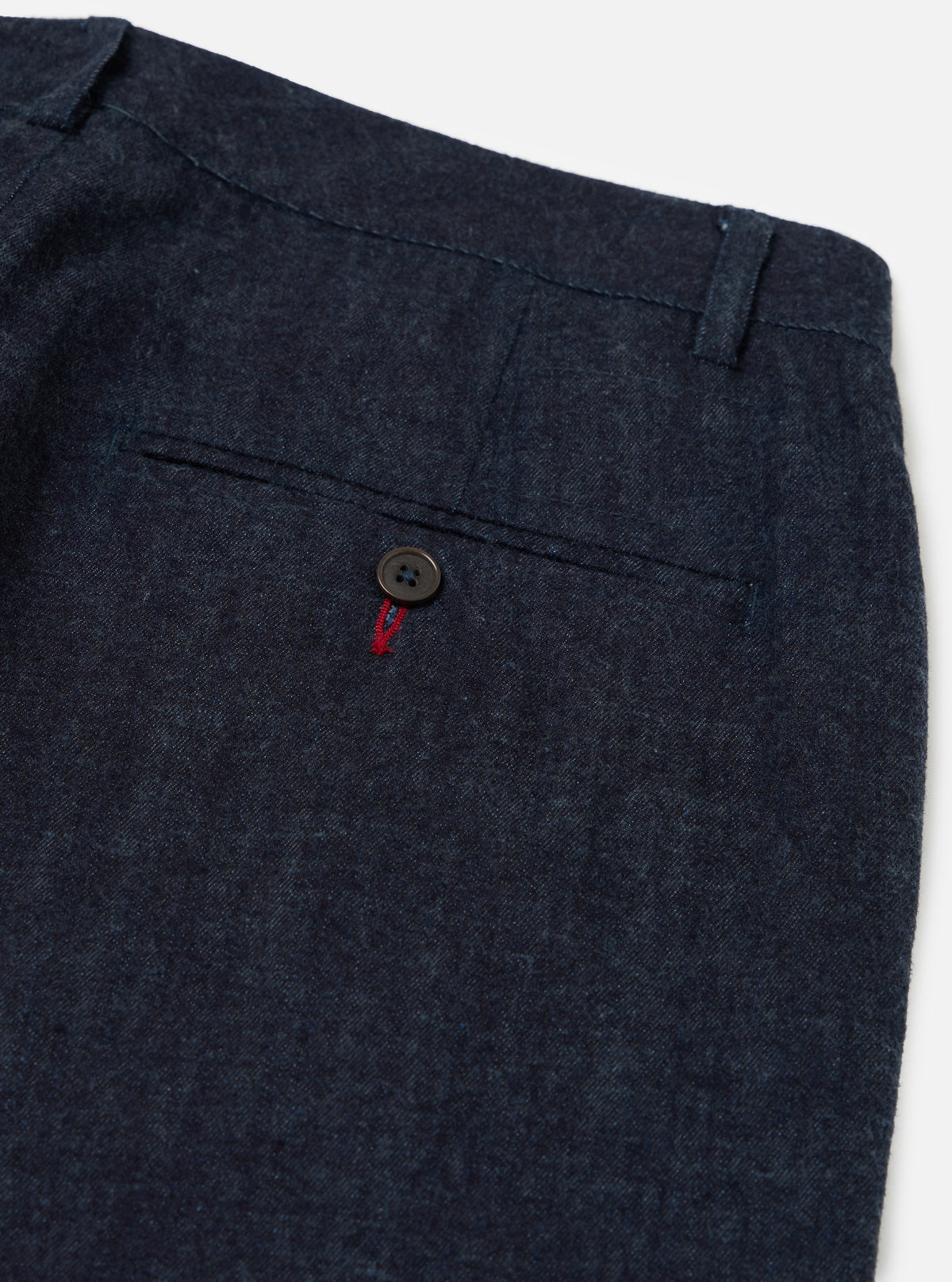 Close-up of Indigo Brushed Denim Military Chino. Dark blue denim fabric with back pocket detail. Button closure with red stitching. Shot on a white background.