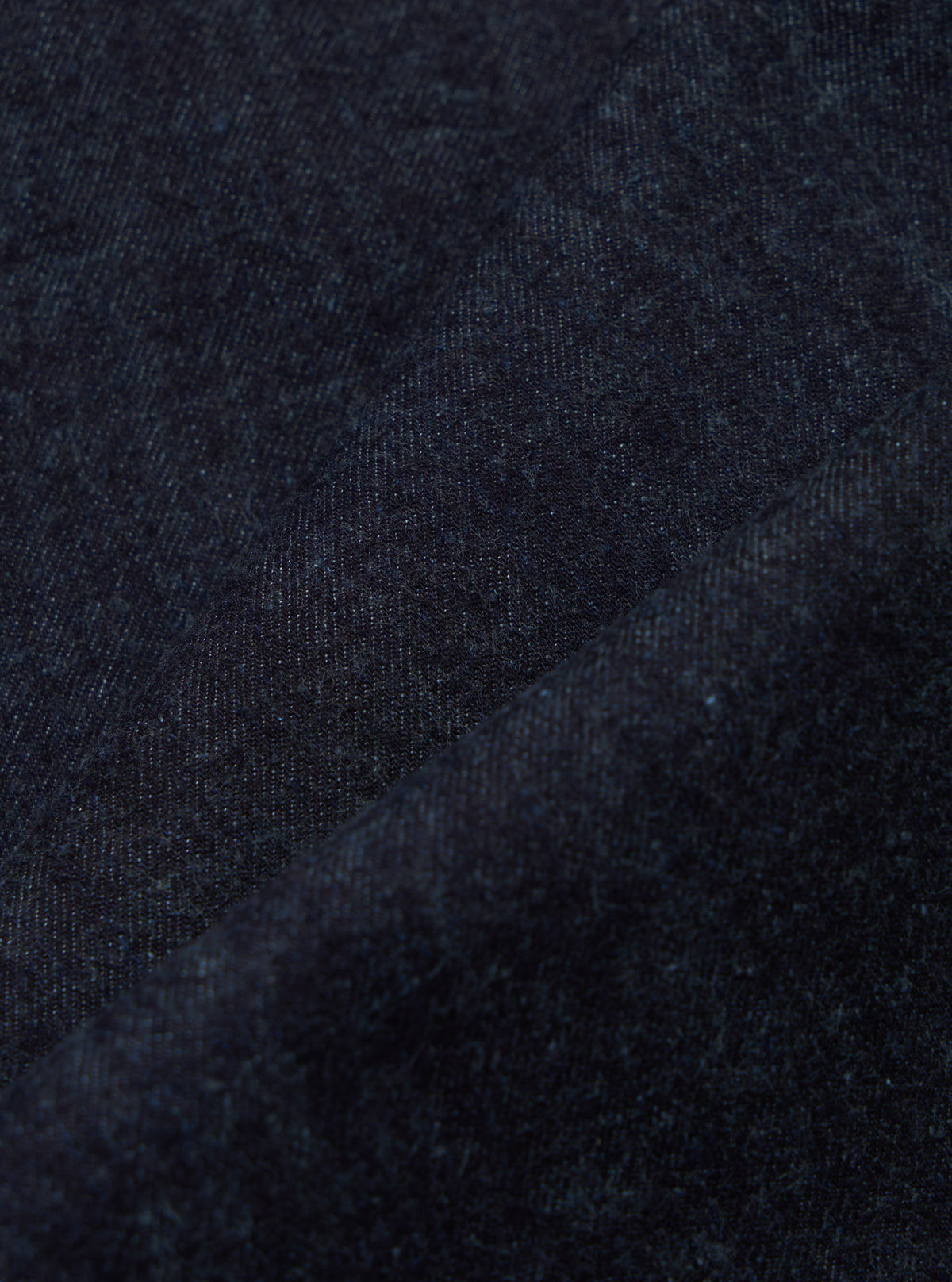 Close-up of indigo brushed denim military chino fabric. The dark blue material is textured and folded, showcasing its weave. Studio shot.