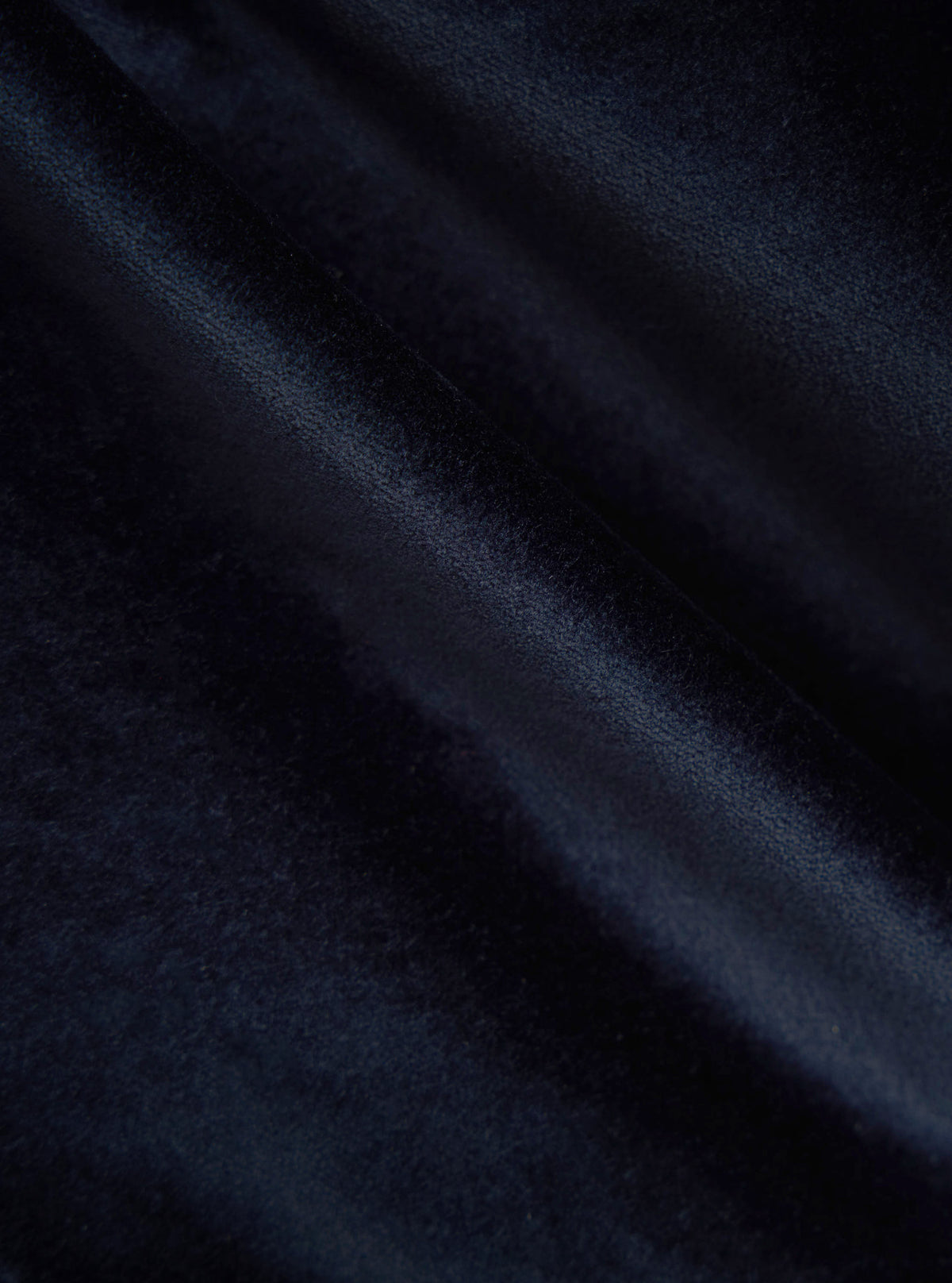 Close-up of the Navy Velveteen Military Chino fabric. The soft, dark blue material is draped to show its texture and quality. The background is a simple, neutral surface.