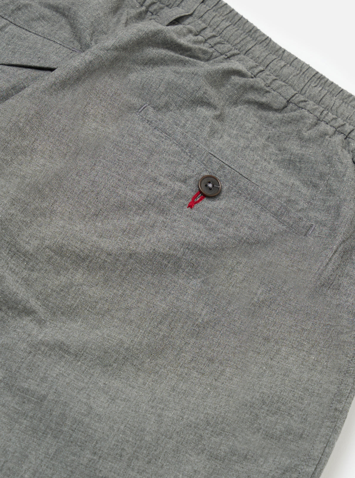 Close-up of the Charcoal Organic Chambray Oxford Pant on a white background, showing the elastic waist, buttoned back pocket, and chambray texture.