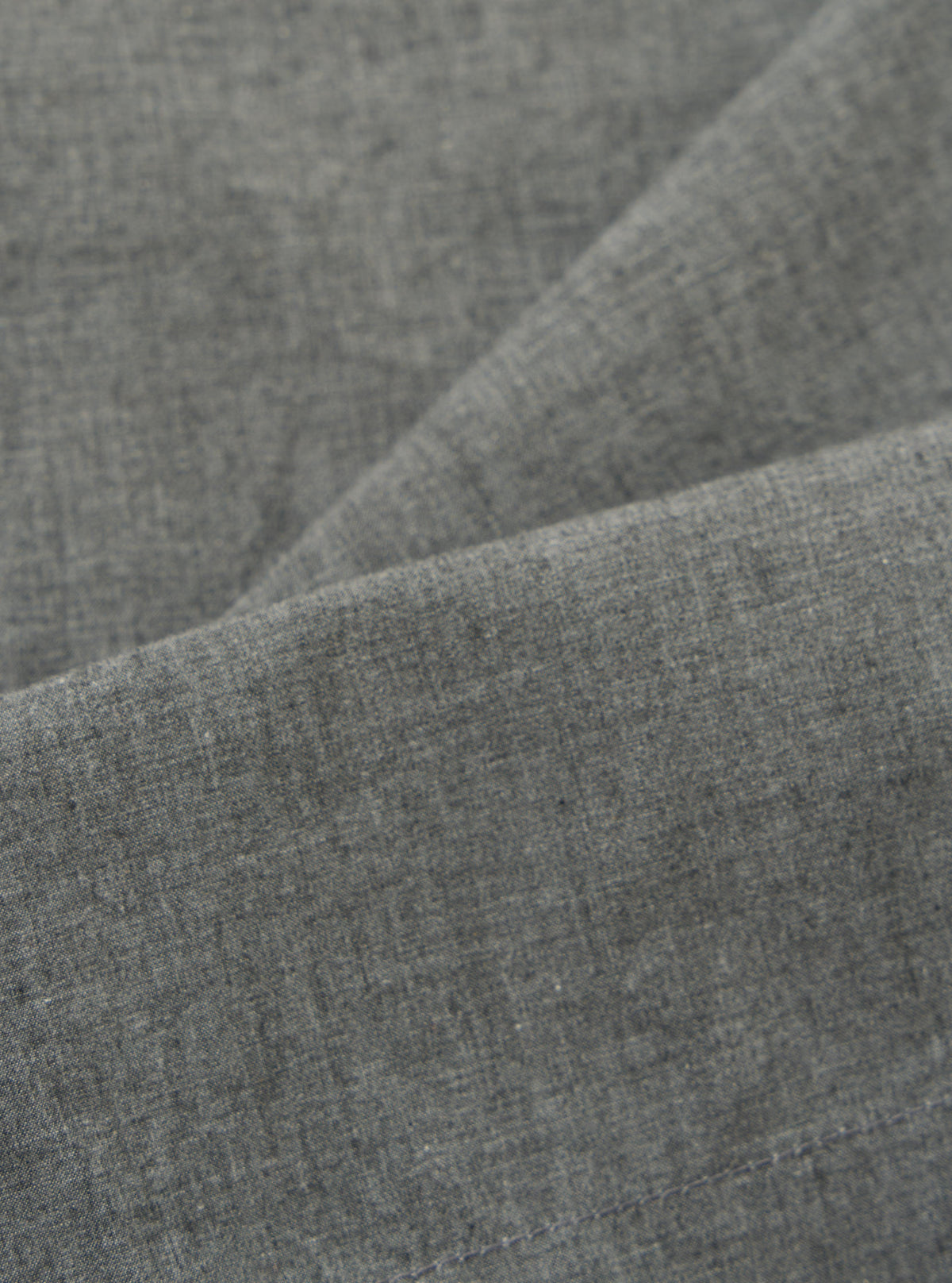 Close-up of the Charcoal Organic Chambray Oxford Pant fabric. The soft, textured material is draped to show its quality. The charcoal color is consistent throughout.