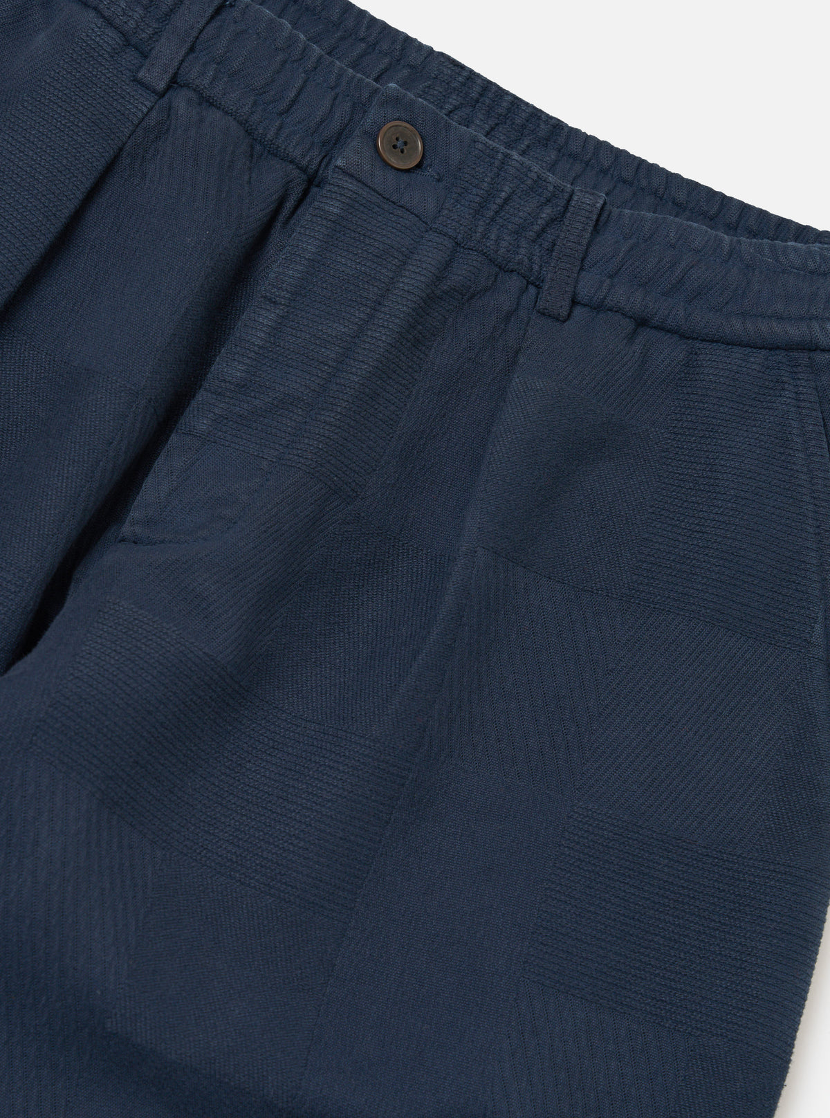 Close-up of the Dark Navy Patchwork Weave Cotton Pleated Track Pant on a white background. The cotton has a subtle patchwork weave texture.